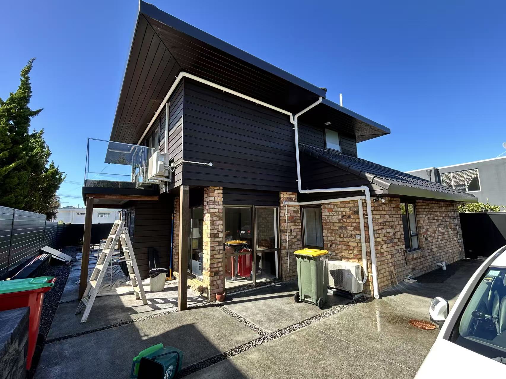 Exterior view of second-storey addition showing new cedar-look cladding over brick base, mid-construction