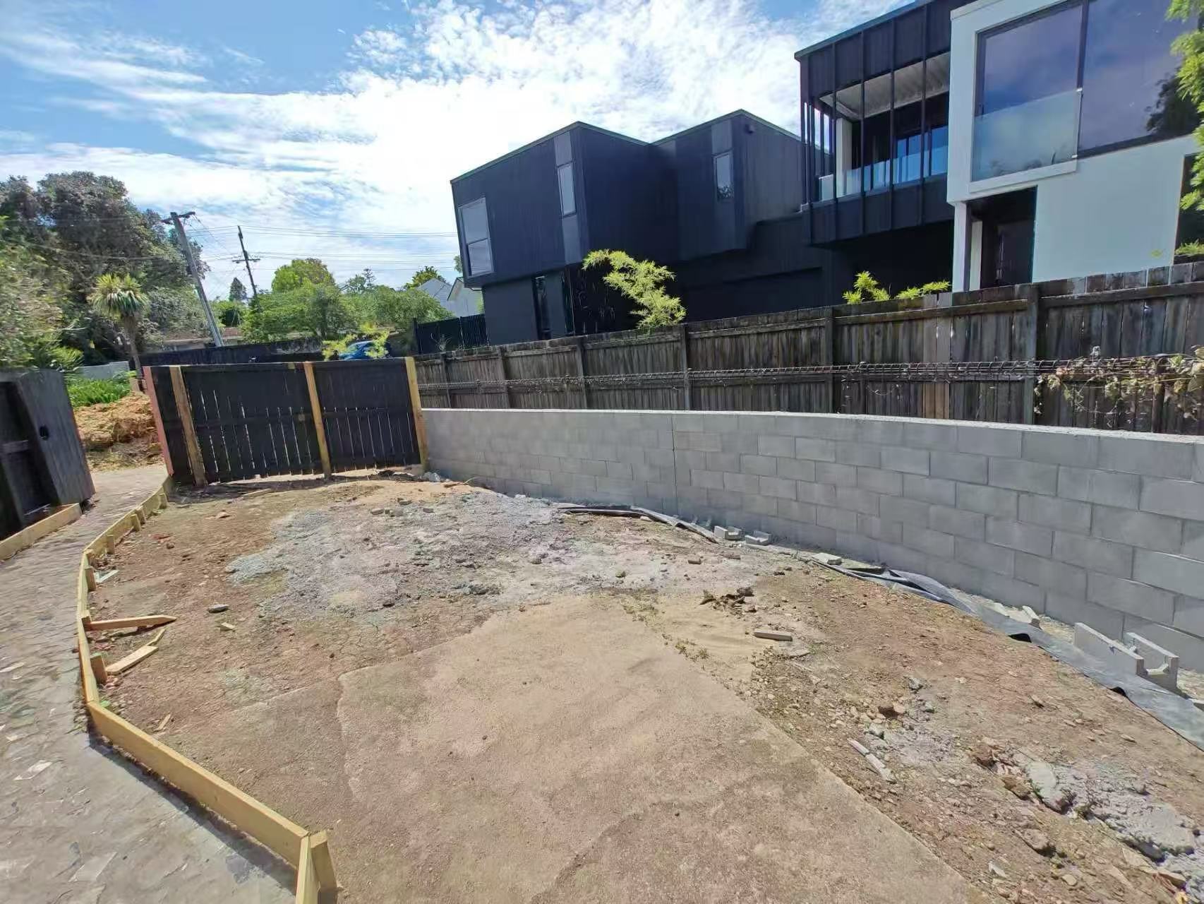 Curved concrete block retaining wall under construction in the rear yard of a modern two-storey home